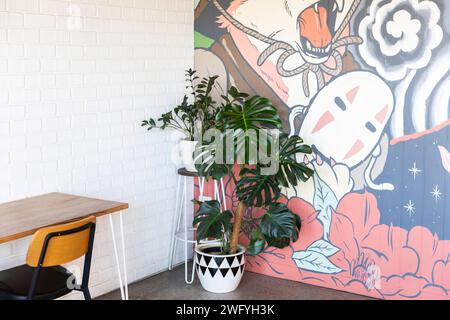 Café-Inneneinrichtung mit stilvollem Design und einer Monstera-Pflanze vor einer lebhaften Graffiti-Wand. Stockfoto