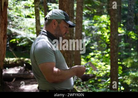 Seitenansicht eines Mannes im Alter von 50 Jahren, der seine Wanderkarte gelesen hat, während er auf dem Timberline Trail in Oregon durch einen Wald wandert. Stockfoto