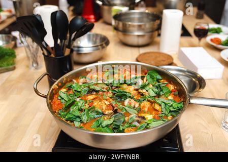 Hausgemachte Tomatensoße mit frischem Basilikum, Gemüse und Gewürzen, die in einer Edelstahlpfanne auf einem Küchenherd gekocht werden. Stockfoto