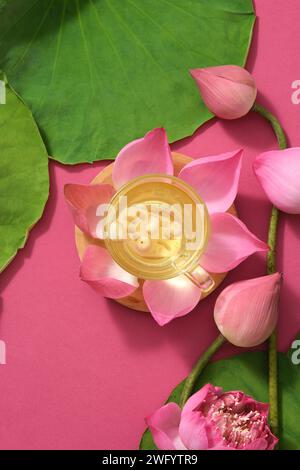 Eine Teetasse mit Lotuswurzel und Lotuskernen, die auf einer Lotusblüte (Nelumbo nucifera) und einige lotusbubs daneben platziert sind. Flache Lagen Stockfoto
