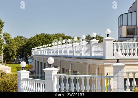 Fragment der Terrasse mit Säulen, Lampen und Geländern. Geländer aus weißem Stein oder Marmor mit Säulen, Balustern und Handläufen Stockfoto