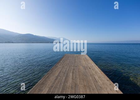 Ein hölzerner Steg an der Promenade in der Nähe von Ohrid am Lake Ohrid in Nordmakedonien, der an einem atemberaubenden sonnigen Tag in das blaue Wasser des Sees ragt. Stockfoto