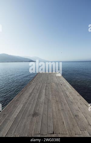 Ein hölzerner Steg an der Promenade in der Nähe von Ohrid am Lake Ohrid in Nordmakedonien, der an einem atemberaubenden sonnigen Tag in das blaue Wasser des Sees ragt. Stockfoto