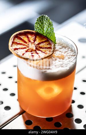 Ein Glas Jungle Bird Cocktail garniert mit getrockneten roten Orangen- und Minzblättern an der Bar. Stockfoto