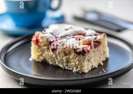 Fruchtiger Pflaumenkuchen auf einem Teller und neben einer Tasse mit Kaffee auf einem Tisch in einem Café. Stockfoto