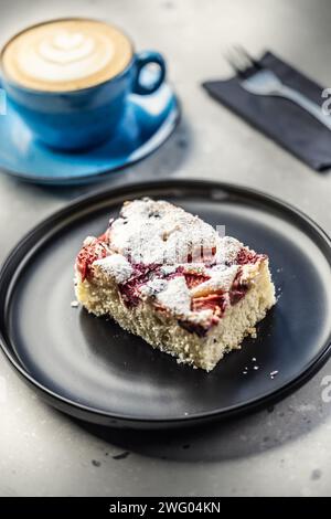 Fruchtiger Pflaumenkuchen auf einem Teller und neben einer Tasse mit Kaffee auf einem Tisch in einem Café. Stockfoto