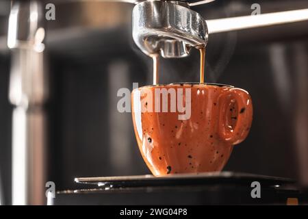 Die Kaffeemaschine macht Kaffee zu einer orangen Tasse. Stockfoto