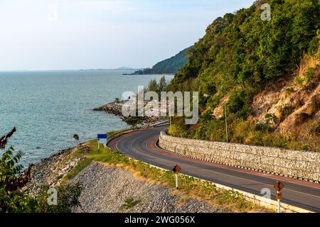 Wunderschöne Aussicht auf den Sonnenuntergang am Noen Nangphaya Aussichtspunkt mit Blick auf das Meer und die gewundene Straße entlang der Küste in Chonburi, Thailand Stockfoto