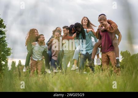 Fröhliche, multirassische Freunde machen Spaß am Huckepack, lachen in einer natürlichen Umgebung und verkörpern die Einheit der Gruppe. Stockfoto