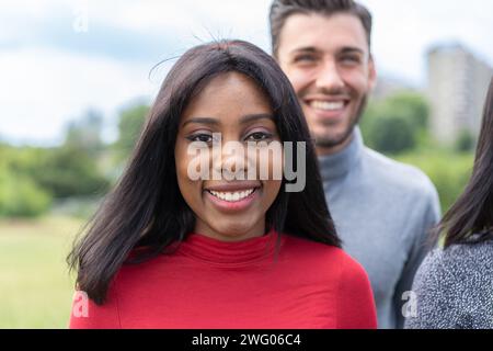 Lebendiges Porträt einer lächelnden jungen Frau mit verschiedenen Freunden in einem Park, das Freude und multikulturelle Beziehungen zeigt. Stockfoto