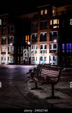 Parkbänke vor beleuchteten Apartments an den historischen Docks von Gloucester bei Nacht im Winter Stockfoto