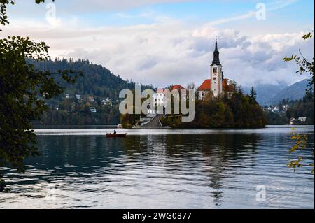 Marienkirche in der Mitte des Bleder Sees in Slowenien, dahinter Berge, Wald, Wolken Stockfoto