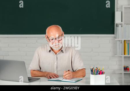 Gealterter pensionierter Lehrer. Porträt eines reifen Lehrers oder Tutors, der an einem Tisch in der Hochschule oder High School arbeitet Stockfoto