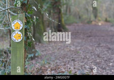 Holzpfosten mit zwei kreisförmigen Schildern, die die Richtung der öffentlichen Fußwege zeigen, geradeaus und links, gekennzeichnet durch Pfeilsymbole nach oben und links Stockfoto