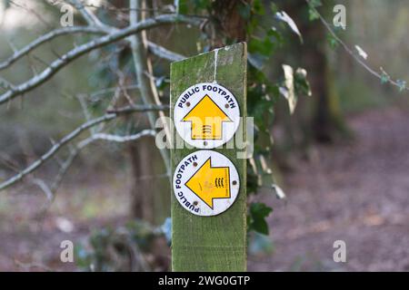 Holzpfosten mit zwei kreisförmigen Schildern, die die Richtung der öffentlichen Fußwege zeigen, geradeaus und links, gekennzeichnet durch Pfeilsymbole nach oben und links Stockfoto