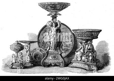 The International Exhibition: Gruppe von Porzellanartikeln von Sir James Duke und Neffen, 1862. '... Ein Dessertservice, zusammen mit einem Hochplateau in Imitation der italienischen Majolika-Ware... das Hochplateau enthält "die Anbetung des Goldenen Kalbes", gemalt von Mr. George Eyre... das Herzstück besteht aus einer reichen Basis, auf dem ein florierter Sockel, umgeben von drei weiblichen Figuren und einer Tazza, die auf dem Sockel liegt. Die Tazza und die Basis sind aus Porzellan und der Sockel und die Figuren aus Parian. Die Tazza ist perforiert und mit Gold-, Magenta- und Malvenbändern angereichert Stockfoto