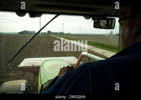 Niederländischer Landwirt fährt eine Kartoffelsämaschine mit Windturbinen im Hintergrund. Stockfoto