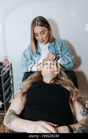 Mädchen mit kurzen blonden Haaren wendet Wimpern auf einen Kunden an, der sich hinlegt Stockfoto