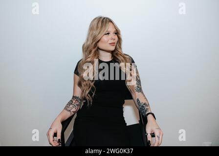 Blondes Mädchen in schwarzem Kleid sitzt und wartet an einer weißen Wand Stockfoto