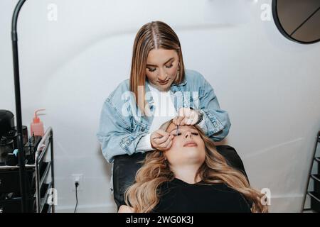 Mädchen mit kurzen blonden Haaren wendet Wimpern auf einen Kunden an, der sich hinlegt Stockfoto