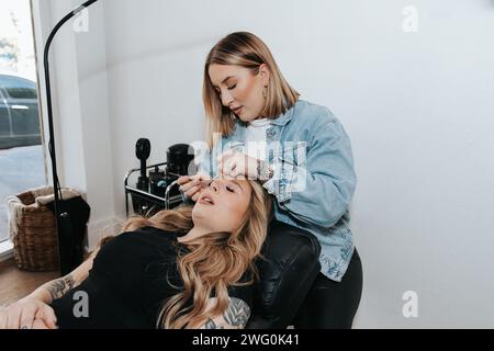 Mädchen mit kurzen blonden Haaren wendet Wimpern auf einen Kunden an, der sich hinlegt Stockfoto
