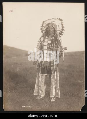 High Hawk, 1907. Das Foto zeigt das Porträt des Hohen Falken in voller Länge, mit Blick auf die Vorderseite, stehend, mit Kriegshaube, zeremonieller Kleidung, Medaillon und einen Putschstock halten. Stockfoto