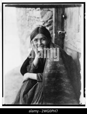 Ein Navaho-Lächeln, 1904. Das Foto zeigt eine Navaho-Frau, die vor der Tür sitzt, mit der rechten Hand auf der Wange, nach vorne gerichtet, lächelnd. Stockfoto