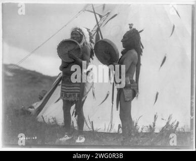 Taten der Tapferkeit singen, um 1908. Zwei Dakota-Männer spielen Handtrommeln außerhalb eines Tipi. Stockfoto