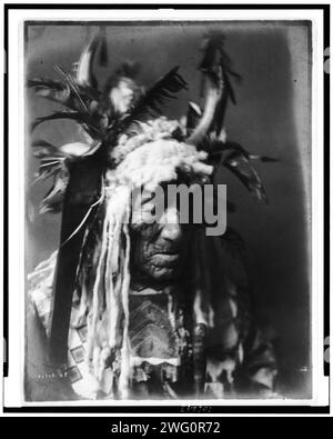 Lean Wolf-Hidatsa, 1908. Lean Wolf, Kopf-und-Schultern-Porträt, nach rechts gerichtet, mit Hornkopfschmuck mit weißem Pelz und dunklen Federn, perlenbesetztes Hemd aus Buckskin. Stockfoto