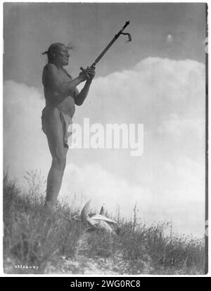 Gebet zum Geheimnis, 1907. Oglala Sioux Mann, Picket Pin, trägt Hosentuch, hält Pfeife mit dem Mundstück nach oben, Büffelschädel zu seinen Füßen. Stockfoto