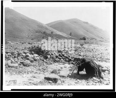 Nez PERC&#xe9; Sweat-Lodge, c1910. Landschaft, verzurrter Pol mit Decke, große glatte Steine im trockenen Flussbett, Haus, Zaun und Hügel im Hintergrund. Stockfoto