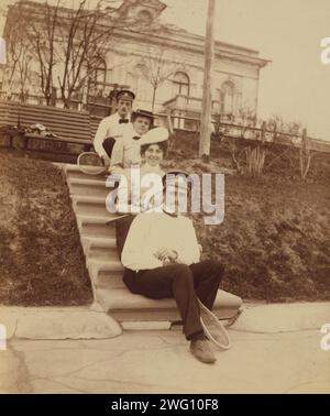 Tennis im Lindholms', Wladiwostok, Russland, 1899. Porträt zeigt Menschen, die in Eleanor Pray's Brief vom 16. Mai 1899 beschrieben werden: „Ich lege ein Foto auf dem Tennisplatz ein – Schramtschenko, Tullie [Lindholm], Lolla [Lindholm] und Fedor Oskarowitsch [stark]. Jeder sagt, es sei eines der besten, das ich je genommen habe, denn jedes Bild ist perfekt, obwohl Wladimir Nikolajewitsch näher an der Vorderseite hätte sein sollen, er sieht so klein auf der obersten Stufe aus. Das Haus ist das Lindholm's und die Straße verläuft zwischen diesem und dem Tennisplatz, und den Hügel von der anderen Seite des Platzes hinunter befindet sich das obere Ende des B Stockfoto