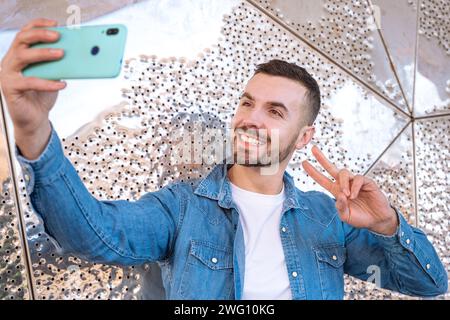 Lächelnder junger Mann, der draußen ein Selbstfoto mit einem Smartphone macht. Stockfoto