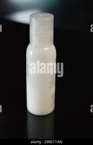 Damenkosmetik, kleine weiße Flasche Hautpflegecreme auf schwarzem Hochglanzhintergrund. Stockfoto