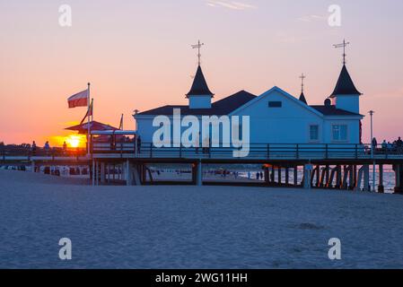 Menschen, die auf einem Pier mit Gebäuden im Sonnenuntergang spazieren, klarer, blauer, wolkenloser Himmel, Pier Ahlbeck im letzten Sonnenlicht, Blick vom Oststrand Stockfoto