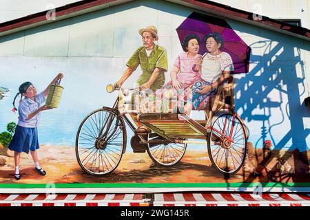 Ein Wandbild in Phuket Town, Phuket, Thailand, das einen alten Trischa-Fahrer mit zwei weiblichen Passagieren und ein junges Mädchen mit einer Tiffin-Box (Lunchbox) zeigt Stockfoto