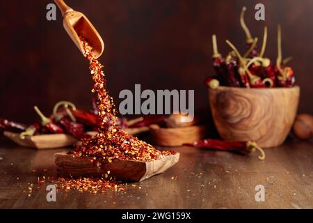 Chiliflocken werden in eine Holzschale gegossen. Chiliflocken und getrocknete Chilischoten auf einem alten Holztisch. Stockfoto