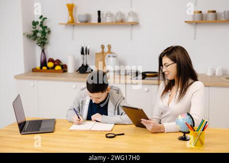 Eine junge Frau hilft einem Jungen beim Unterricht mit einem Tablet und einem Globus. Ein Schüler macht seine Hausaufgaben mit Hilfe eines Tutors. Stockfoto