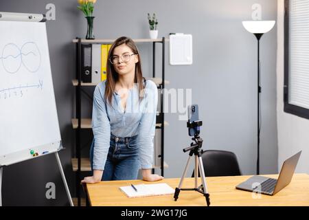 Junge Frau Mentorin nimmt Präsentationen auf, Webinar über Smartphone auf Stativ stehend, Lehrer Coach erklärt, hält Online-Unterricht, mit Telefon-Webc Stockfoto