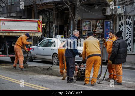 Arbeiter in orangefarbenen Uniformen und Schutzausrüstungen reparieren und reparieren beschädigte Straßen in der Innenstadt von Großstädten, schwere Maschinen und schmutzige Arbeiten Stockfoto