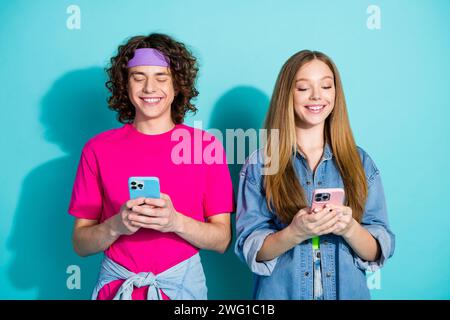 Porträt von Schwester und Bruder Teenager Mädchen mit Jungen, der süchtig chtigt mit Smartphones kommuniziert isoliert auf blauem Hintergrund Stockfoto