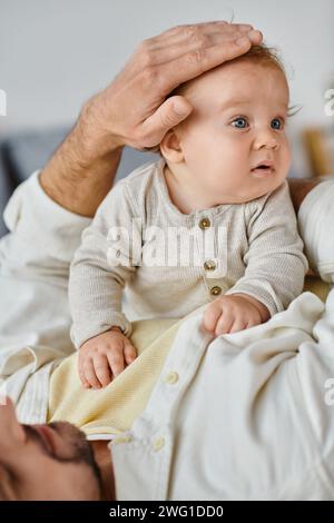 Alleinerziehender Vater mit lockigen Haaren und Bart, der die Haare seines kleinen Jungen im Schlafzimmer streichelt, Liebe und Pflege Stockfoto