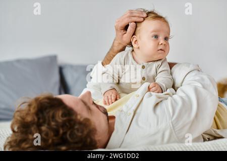 Alleinerziehender Vater mit lockigen Haaren und Bart, der die Haare seines kleinen Sohnes im Schlafzimmer streichelt, Liebe und Pflege Stockfoto