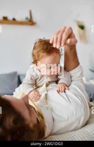 Mann mit lockigen Haaren und Bart, der sich mit seinem kleinen Sohn auf einem Bett umarmt und sich zwischen Vater und Kind verbündet Stockfoto