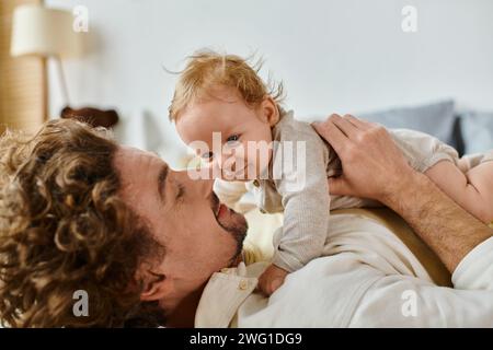 Glücklicher Mann mit lockigen Haaren und Bart, der sich mit seinem kleinen Sohn im Schlafzimmer umschließt, Liebe und Pflege Stockfoto