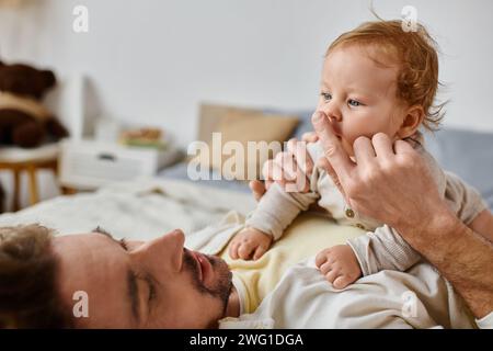 Mann mit lockigen Haaren und Bart, der die Nase seines Kindes berührt, Band zwischen Vater und Kind Stockfoto