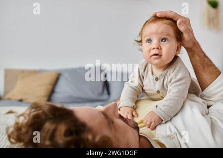 Mann mit lockigen Haaren und Bart streichelt Haare mit seinem kleinen Sohn mit blauen Augen im Schlafzimmer Stockfoto