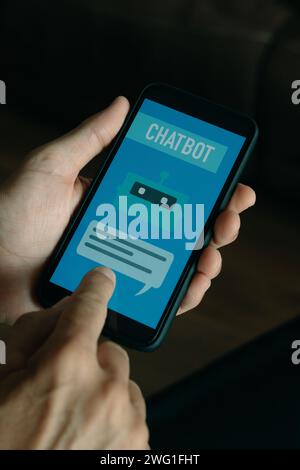 Nahaufnahme eines jungen Mannes drinnen mit einem simulierten Chatbot auf seinem Smartphone, der den Text-Chatbot auf seinem Bildschirm liest Stockfoto