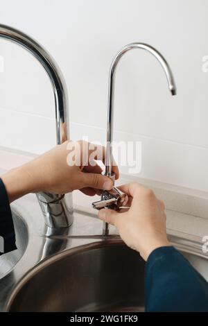 Nahaufnahme eines kaukasischen Mannes, der blaue Overalls trägt und einen zusätzlichen Wasserhahn in einem Spülbecken aus Metall installiert Stockfoto