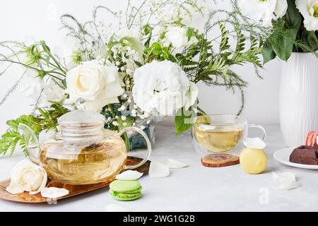 Ästhetische Tischeinstellung. Grüner Tee, Makronen-Desserts, Schokolade, weißes Bouquet - Zeit für sich, langsam lebendiges Konzept Stockfoto